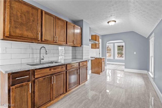 kitchen with sink, light stone counters, a textured ceiling, decorative backsplash, and vaulted ceiling