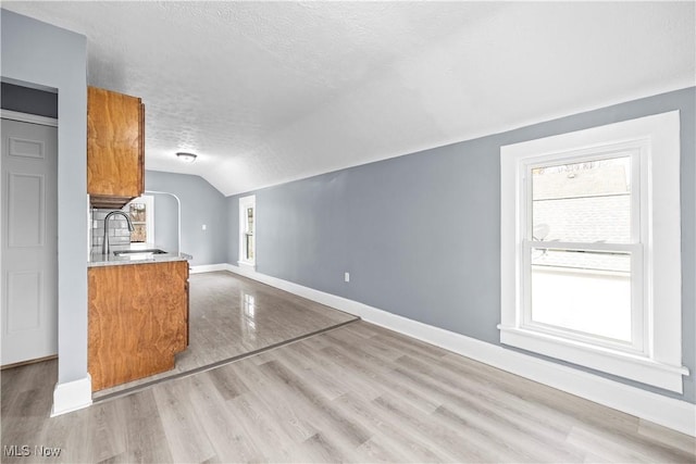 interior space with lofted ceiling, light hardwood / wood-style floors, sink, and a textured ceiling