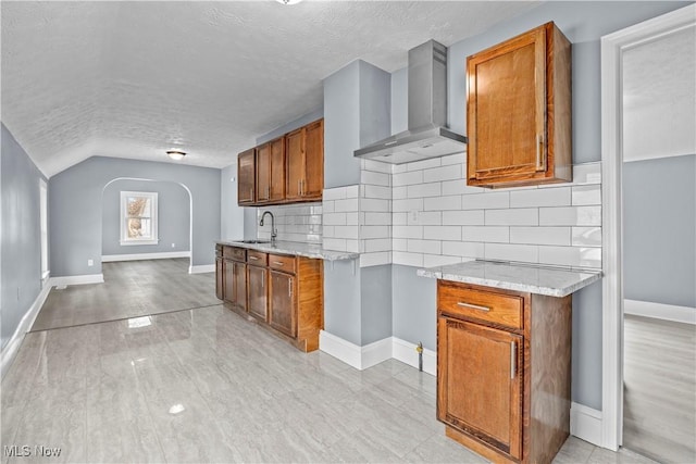 kitchen with lofted ceiling, sink, backsplash, a textured ceiling, and wall chimney exhaust hood