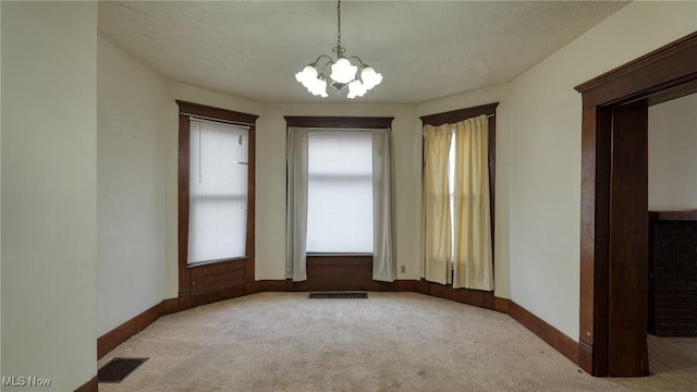 carpeted empty room featuring a notable chandelier and a textured ceiling