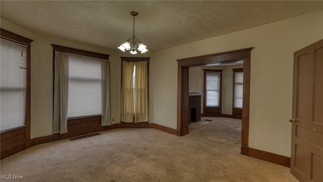 carpeted spare room with a textured ceiling, a fireplace, and a chandelier