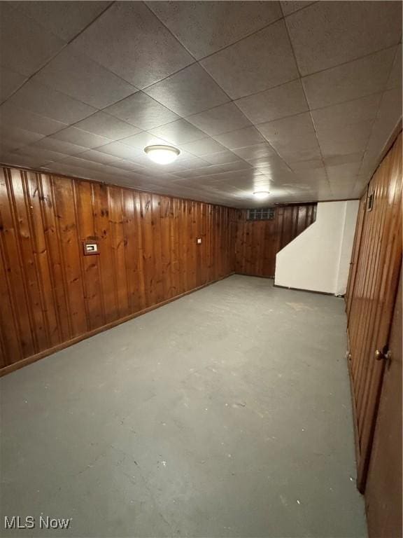 basement with a paneled ceiling and wood walls