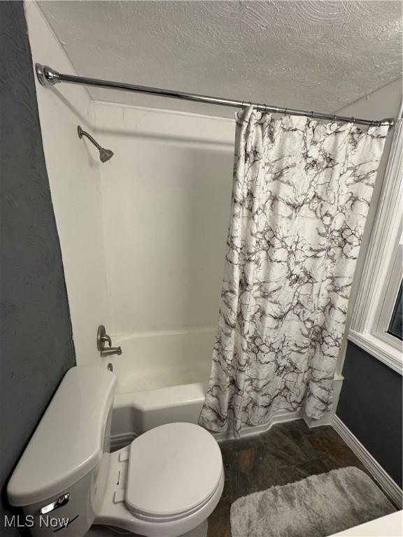 bathroom featuring shower / bath combination with curtain, toilet, and a textured ceiling