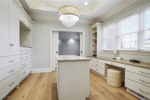 spacious closet featuring a notable chandelier, a tray ceiling, built in desk, and light wood-type flooring