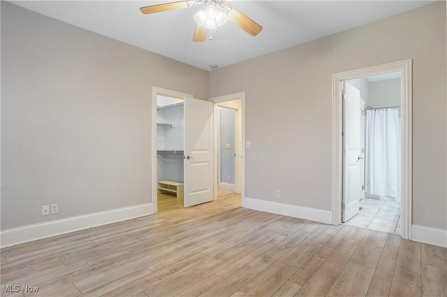 unfurnished bedroom featuring ensuite bath, light hardwood / wood-style flooring, ceiling fan, a spacious closet, and a closet