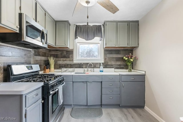 kitchen with appliances with stainless steel finishes, tasteful backsplash, sink, ceiling fan, and light wood-type flooring