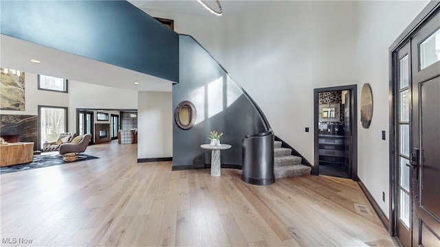 foyer with a towering ceiling, a fireplace, and light hardwood / wood-style floors