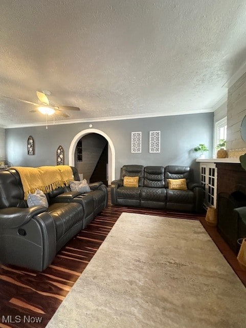 living room featuring dark hardwood / wood-style floors, a fireplace, ceiling fan, crown molding, and a textured ceiling