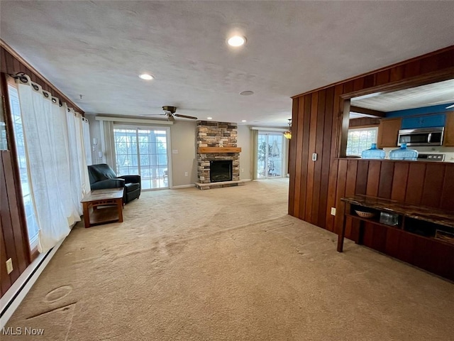 unfurnished living room with carpet floors, wood walls, a healthy amount of sunlight, and baseboard heating