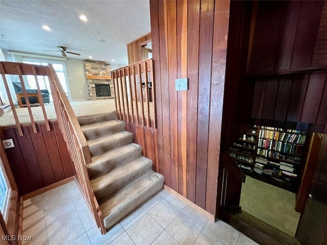 stairs with ceiling fan, wooden walls, and a fireplace