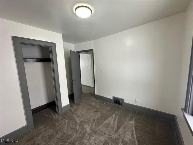 unfurnished bedroom with dark colored carpet and a closet