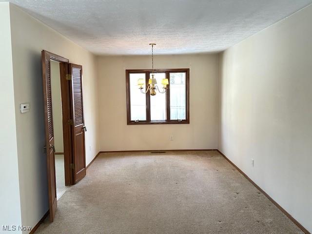 spare room with light colored carpet, a textured ceiling, and a notable chandelier