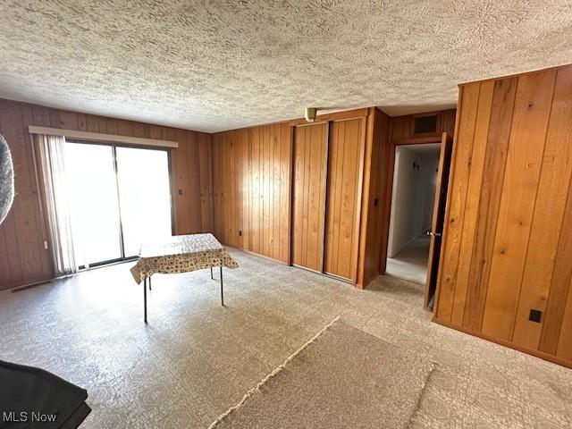 misc room featuring light carpet, wooden walls, and a textured ceiling