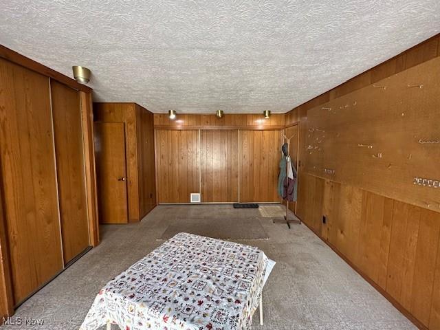 bedroom featuring a textured ceiling, light carpet, and wood walls