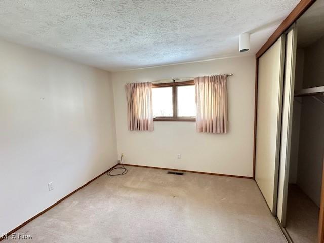 unfurnished bedroom with light colored carpet, a closet, and a textured ceiling