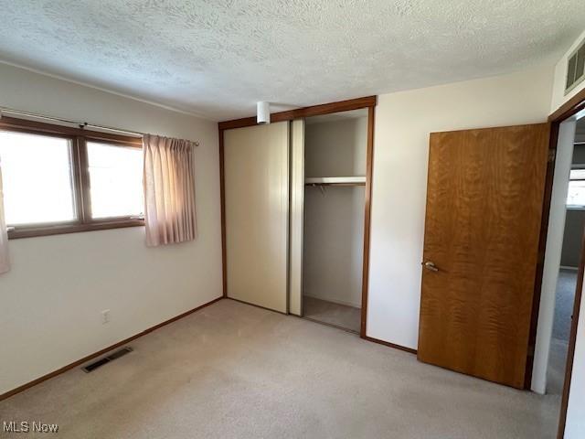 unfurnished bedroom with light colored carpet, a textured ceiling, and a closet