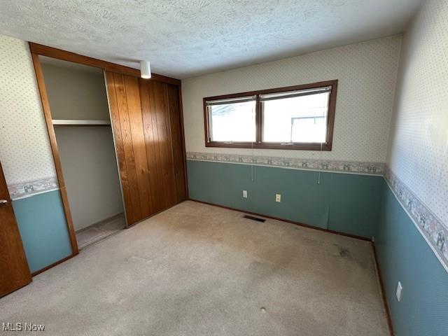 unfurnished bedroom with light colored carpet, a closet, and a textured ceiling