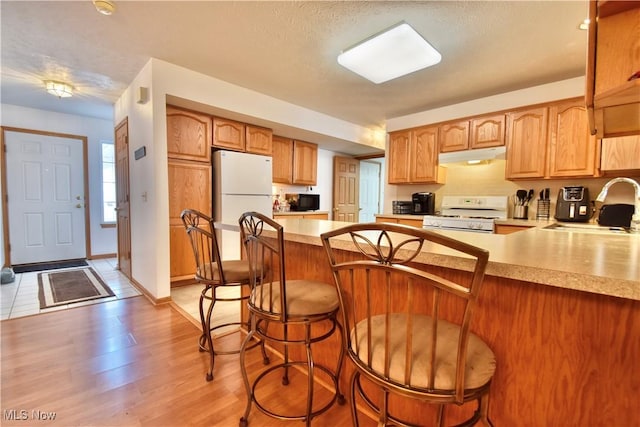 kitchen featuring sink, a kitchen breakfast bar, light hardwood / wood-style floors, kitchen peninsula, and white appliances