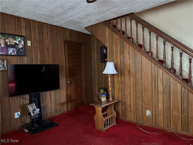 living room featuring wooden walls, dark carpet, and a textured ceiling