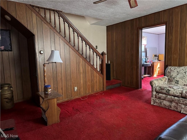 living room featuring dark colored carpet, ceiling fan, a textured ceiling, and wood walls