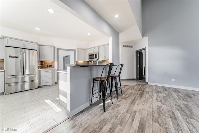 kitchen featuring decorative backsplash, gray cabinets, stainless steel appliances, and a breakfast bar area