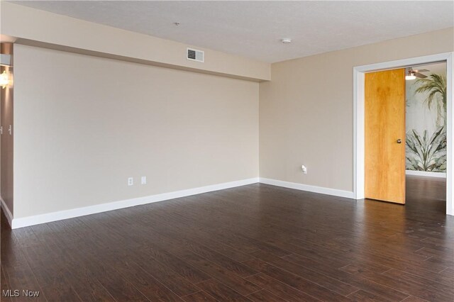 empty room featuring dark wood-style flooring, visible vents, and baseboards