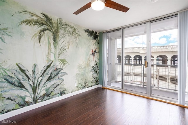 empty room featuring expansive windows, ceiling fan, and hardwood / wood-style floors