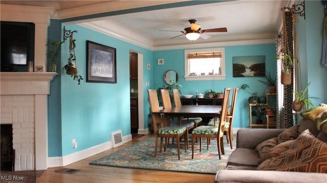 interior space with a brick fireplace, hardwood / wood-style flooring, ornamental molding, and ceiling fan