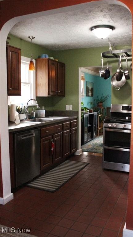 kitchen featuring sink, decorative light fixtures, dark brown cabinets, a textured ceiling, and appliances with stainless steel finishes