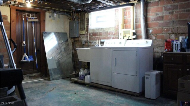 basement featuring sink, electric panel, washer and dryer, and brick wall