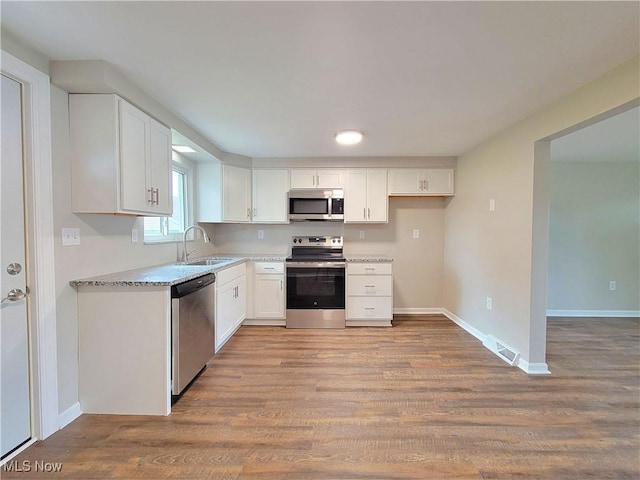 kitchen featuring sink, light stone counters, appliances with stainless steel finishes, light hardwood / wood-style floors, and white cabinets