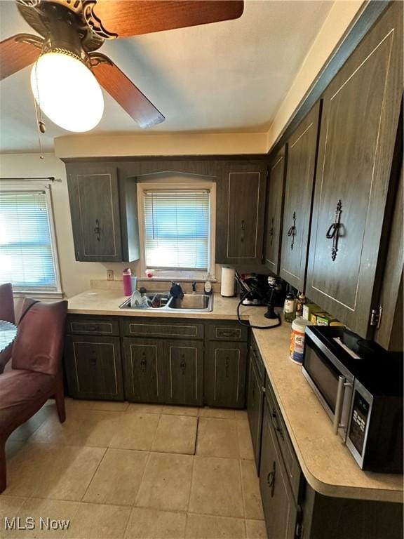 kitchen featuring dark brown cabinetry, sink, light tile patterned floors, and ceiling fan