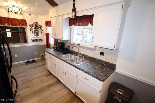 kitchen with sink, white cabinetry, tasteful backsplash, black fridge, and light wood-type flooring