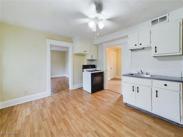 kitchen with light wood-type flooring, gas range oven, sink, and white cabinets