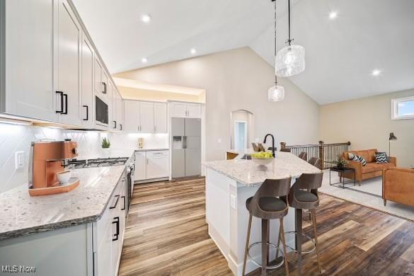 kitchen with refrigerator with ice dispenser, a kitchen island with sink, light stone countertops, white cabinets, and decorative light fixtures