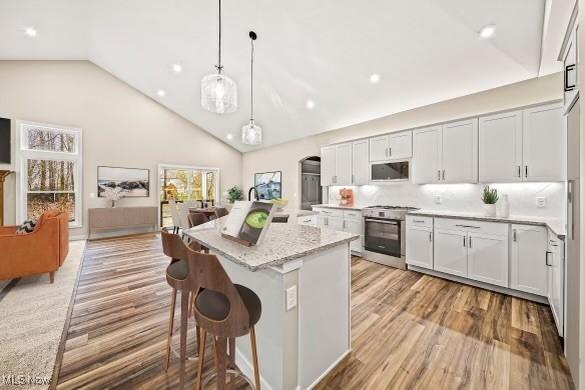 kitchen with decorative light fixtures, a breakfast bar area, a center island, stainless steel gas range oven, and light stone countertops