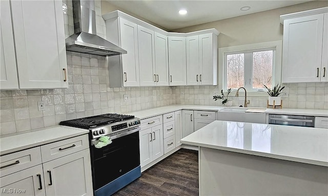 kitchen featuring wall chimney range hood, appliances with stainless steel finishes, white cabinetry, tasteful backsplash, and dark hardwood / wood-style flooring