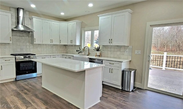 kitchen featuring wall chimney range hood, white cabinetry, a center island, stainless steel gas range oven, and dark hardwood / wood-style flooring