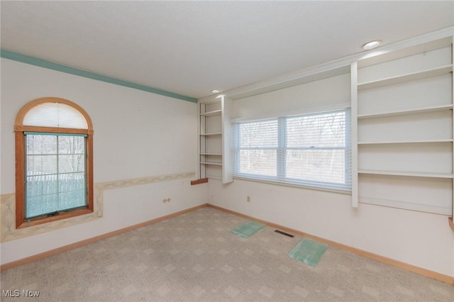 unfurnished room featuring crown molding, built in shelves, and light colored carpet