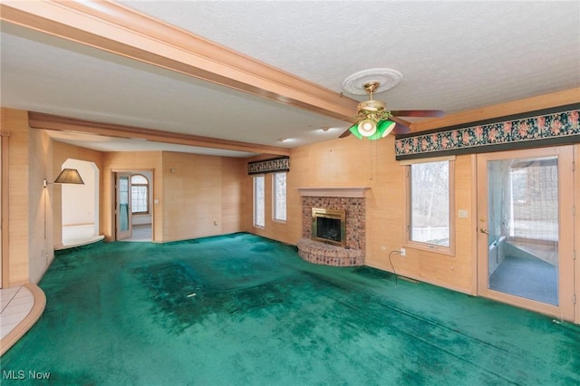 unfurnished living room with a fireplace, beamed ceiling, ceiling fan, dark carpet, and a textured ceiling