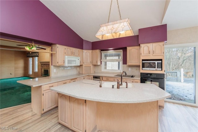 kitchen featuring stainless steel microwave, a center island with sink, oven, and light brown cabinetry