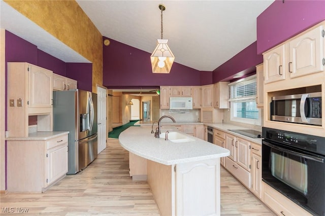 kitchen with sink, hanging light fixtures, light hardwood / wood-style floors, black appliances, and a center island with sink