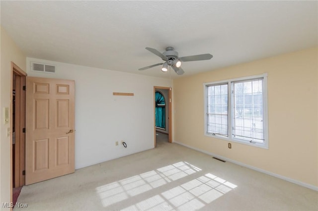 spare room featuring ceiling fan, light carpet, and a walk in closet