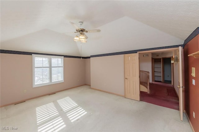 unfurnished bedroom featuring ceiling fan, light colored carpet, vaulted ceiling, and a textured ceiling