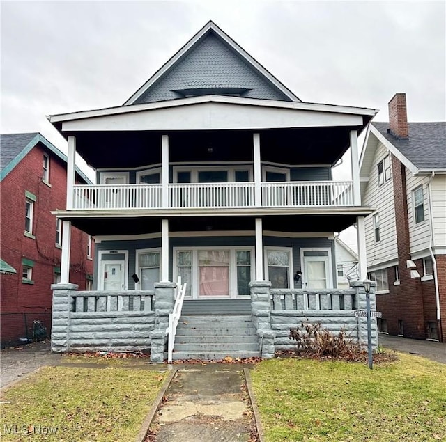 view of front facade with a balcony, a porch, and a front lawn