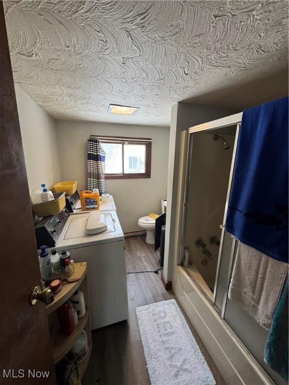 full bathroom with washing machine and clothes dryer, toilet, bath / shower combo with glass door, a textured ceiling, and hardwood / wood-style flooring