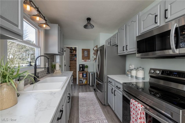 kitchen with sink, gray cabinetry, light stone counters, light hardwood / wood-style flooring, and appliances with stainless steel finishes