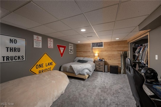 bedroom featuring carpet, a paneled ceiling, and wood walls