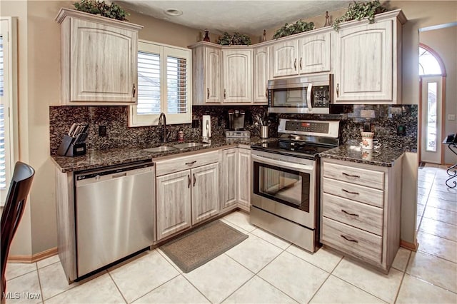 kitchen with sink, light brown cabinets, appliances with stainless steel finishes, dark stone counters, and backsplash