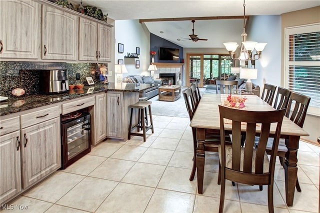 tiled dining area featuring wine cooler, ceiling fan with notable chandelier, a fireplace, and vaulted ceiling